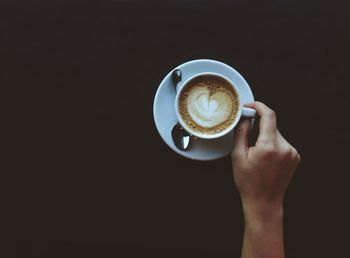 Cropped hand holding coffee with saucer and spoon. dark copyspace. espresso in a cup. 