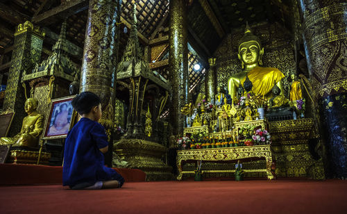 Boy praying against statue of buddha