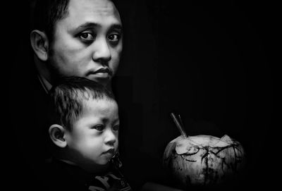 Close-up of father and son with coconut against black background