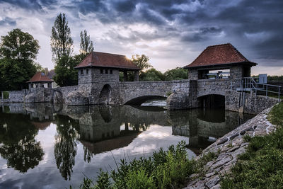 Arch bridge over river by buildings against sky