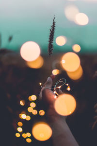 Cropped image of hand holding illuminated string lights during sunset