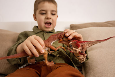 Little and cute caucasian boy playing with dinosaurs at home. 