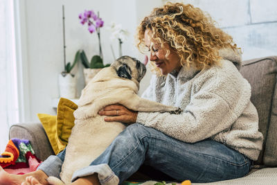 Side view of woman playing with pug on bed at home