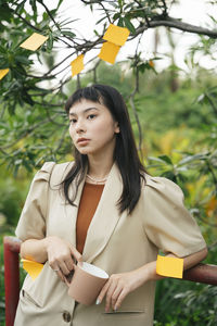 Young woman looking away while standing against plants