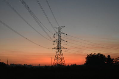 Low angle view of silhouette electricity pylons on field against sky at sunset