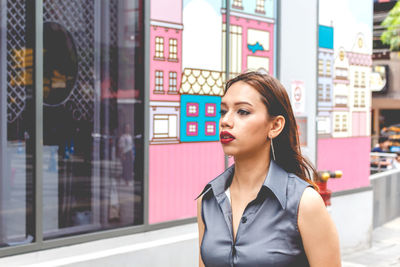 Beautiful young woman looking away by building in city