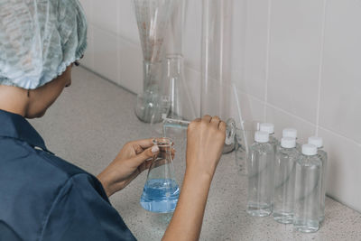 Woman in protective cap checks water quality, glass tube filled, chemical, research, analysis in lab