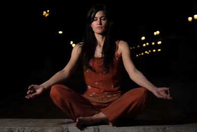 Mid adult woman doing yoga on retaining wall at night