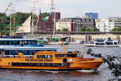 Boats sailing on river by buildings in city against sky