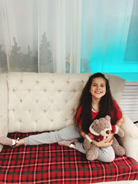 Portrait of smiling girl sitting on sofa with stuffed toy