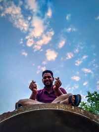 Portrait of happy young man holding camera against sky