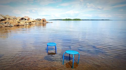 Deck chairs on rocks by lake against sky