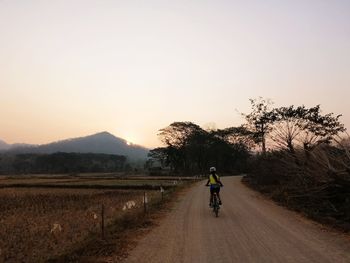 Rear view of person riding bicycle on road against sky