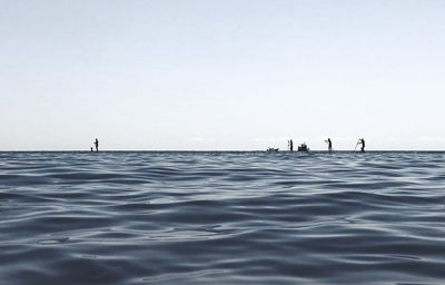 Silhouette people on sea against clear sky