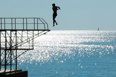Silhouette man jumping in sea on sunny day