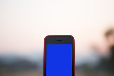 Close-up of mobile phone against sky