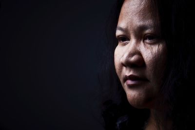 Close-up of thoughtful mid adult woman looking away against black background