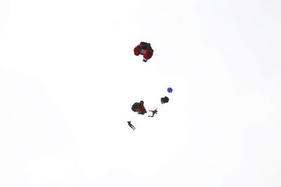 Low angle view of men paragliding against clear sky