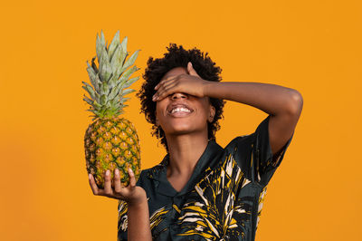 Young african american woman with short hair dressed in a summer shirt posing with pineapple