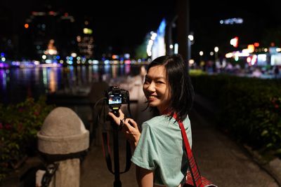 Portrait of smiling woman photographing from camera in city at night