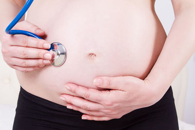 Midsection of pregnant woman examining belly at home