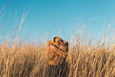 Headless person standing amidst plants on field against sky