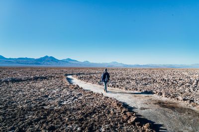 Man walking on landscape against clear blue sky