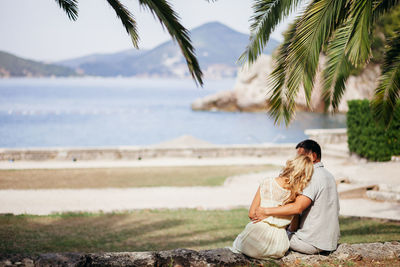 Couple sitting on palm tree by sea against sky