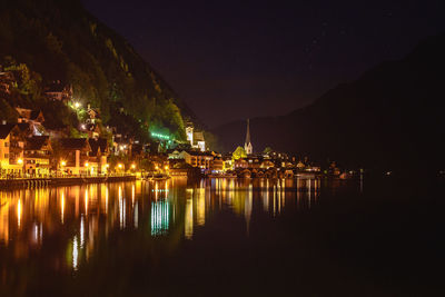 Illuminated city by lake against sky at night