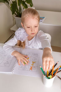 A girl student sits at a desk in the classroom and paints a picture with pencils. back to school 