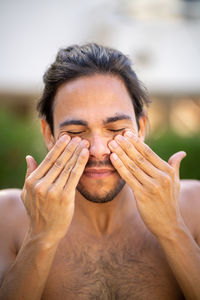 Close-up portrait of shirtless man putting himself sun protection