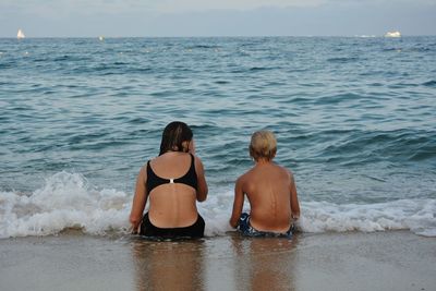 Two children sitting on the beach in a wave