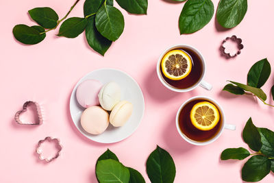 Tea brake set - two cups of tea with lemon and rose leaves with marshmallows on a pink background.