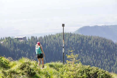 Rear view of female hiker standing on grassy cliff against forest