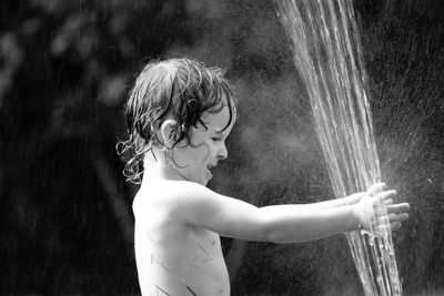 Side view of shirtless boy playing with fountain water