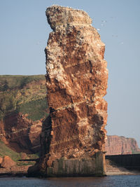 Rock formation by sea against clear sky