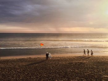 People playing on beach against sky during sunset