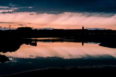 Scenic view of lake against cloudy sky during sunset