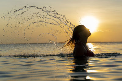 Woman splashing water against sea during sunset