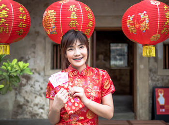 Smiling woman holding envelope with paper currency by red lantern