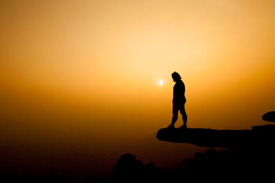 Silhouette of woman standing on cliff against sky during sunset