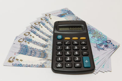 High angle view of calculator on paper currency over white background