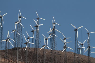 Windmills on landscape against clear blue sky