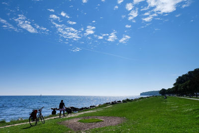 Rear view of woman walking on field by sea against blue sky