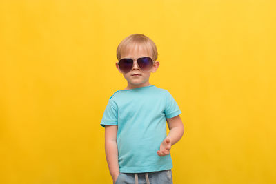Boy wearing sunglasses standing against yellow background
