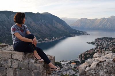 Woman sitting on rock by lake against sky