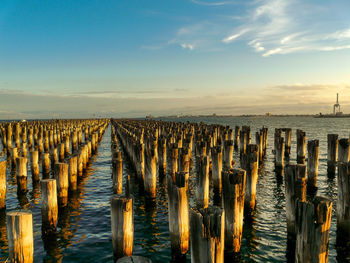 Wooden posts in sea against sky at sunset