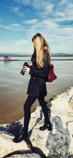 Side view of woman with camera standing on retaining wall