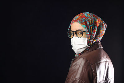 Portrait of woman in hijab standing against black background