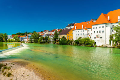 Buildings by river against clear blue sky